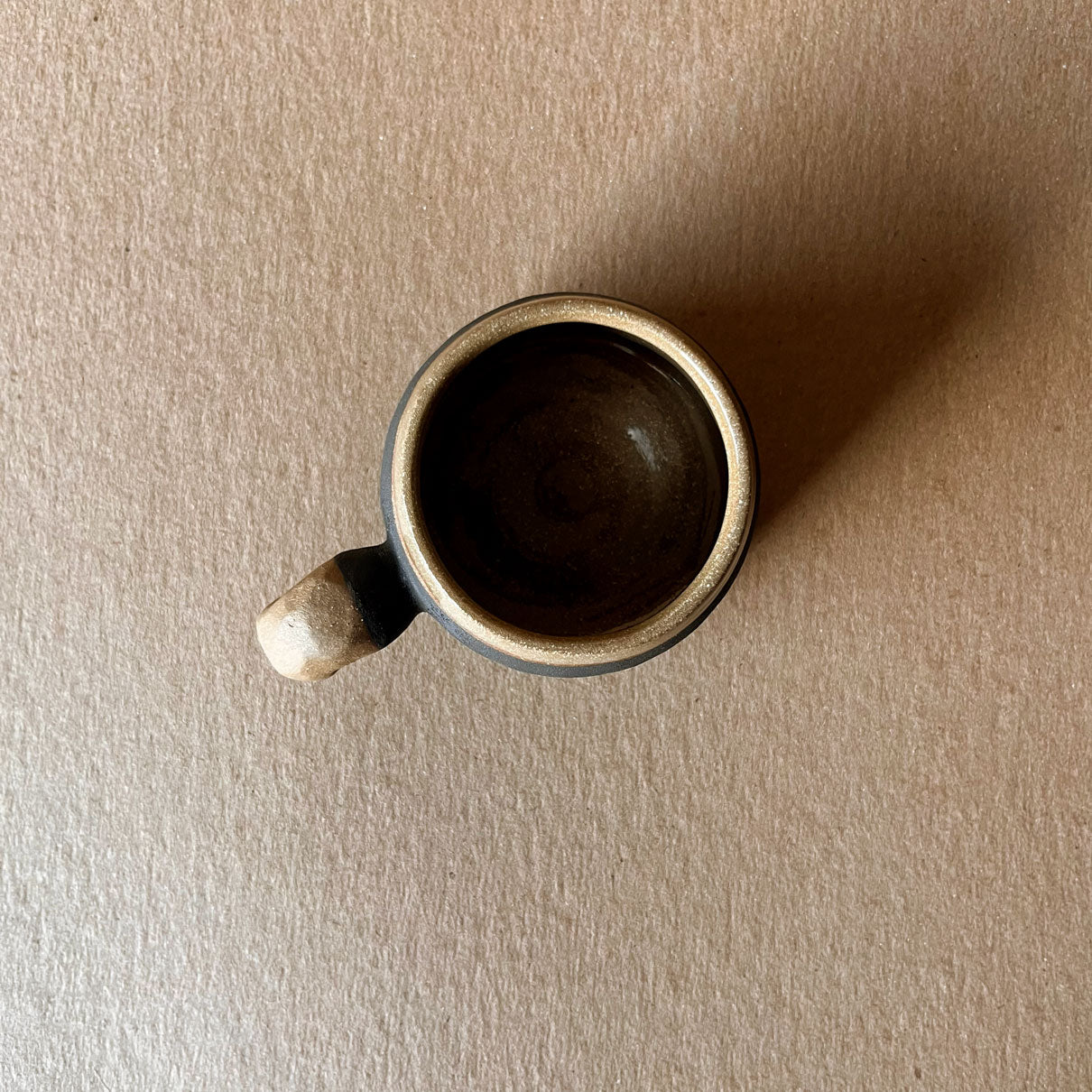An elegant billowing body form in brown stoneware, featuring a hammered raw texture. Black underglazed exterior that has a volcanic rock texture, with a clear glazed lip and interior.