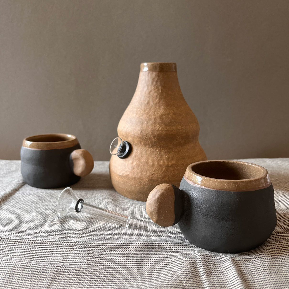 An elegant billowing body form in brown stoneware, featuring a hammered raw texture. Black underglazed exterior that has a volcanic rock texture, with a clear glazed lip and interior.