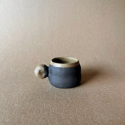 An elegant billowing body form in brown stoneware, featuring a hammered raw texture. Black underglazed exterior that has a volcanic rock texture, with a clear glazed lip and interior.