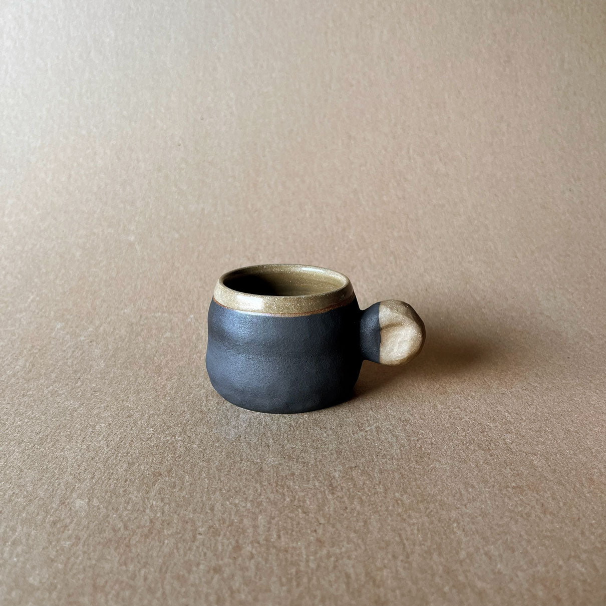 An elegant billowing body form in brown stoneware, featuring a hammered raw texture. Black underglazed exterior that has a volcanic rock texture, with a clear glazed lip and interior.