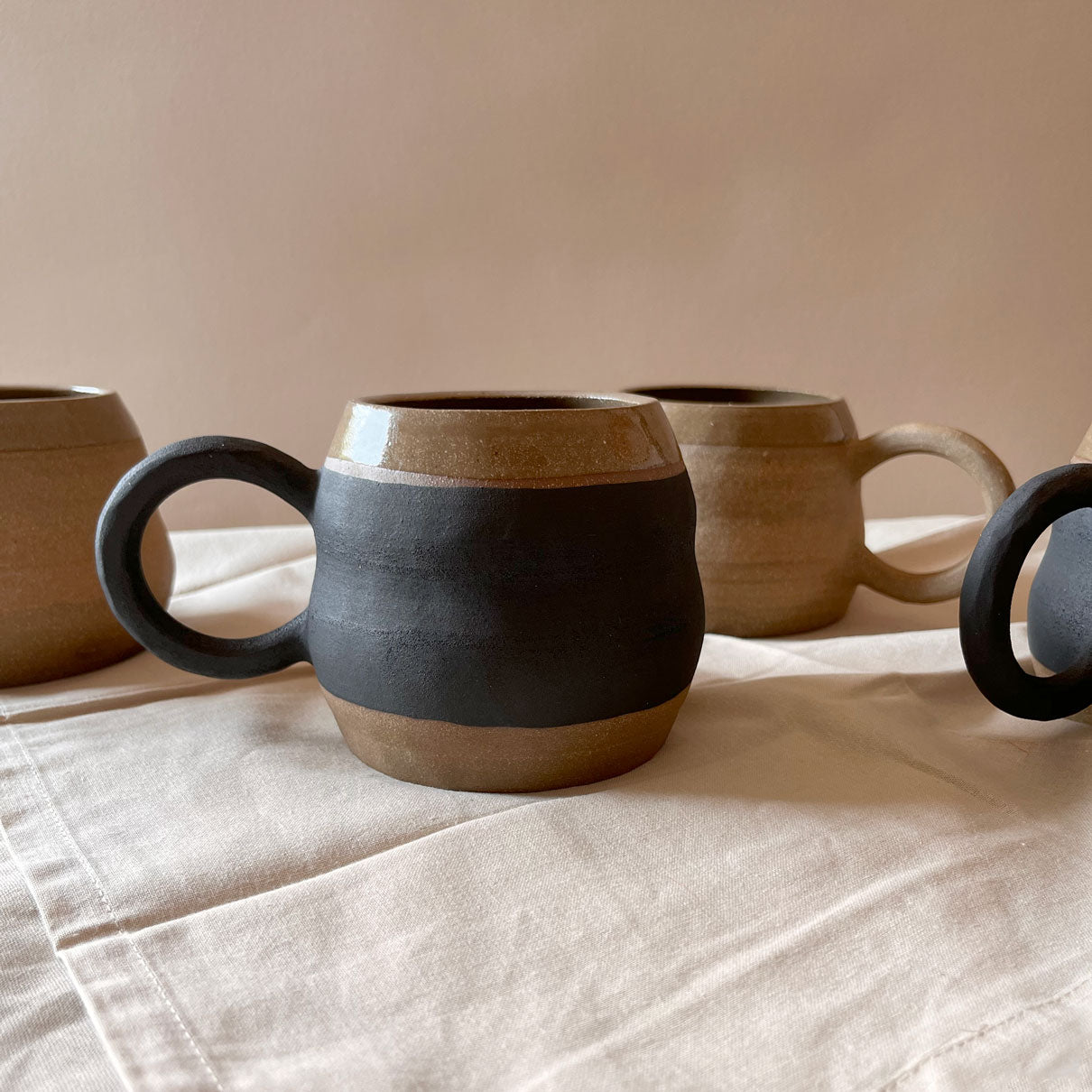 An elegant billowing body form in brown stoneware, featuring a hammered raw texture. Black underglazed exterior that has a volcanic rock texture, with a clear glazed lip and interior.