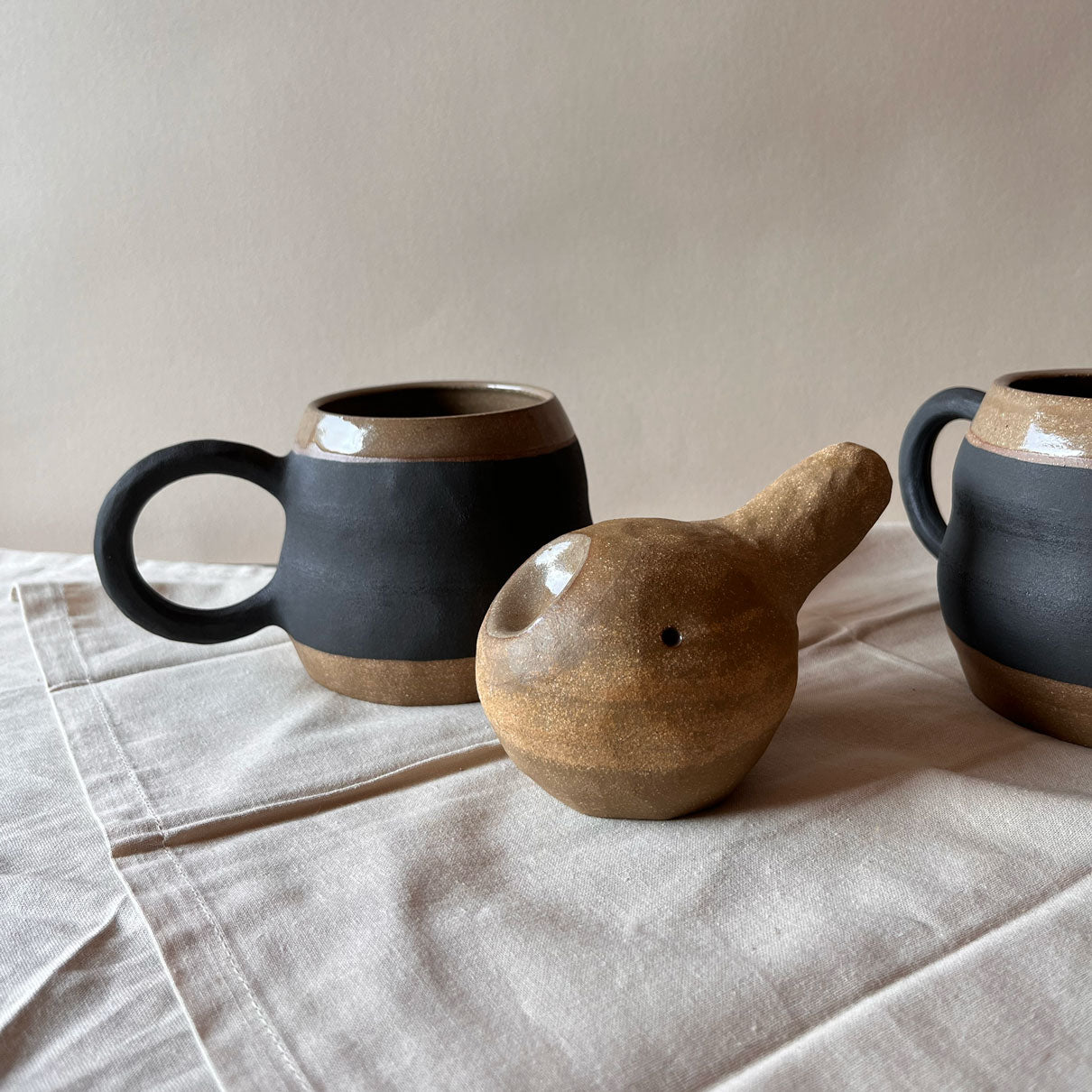 An elegant billowing body form in brown stoneware, featuring a hammered raw texture. Black underglazed exterior that has a volcanic rock texture, with a clear glazed lip and interior.