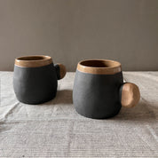An elegant bulbous body form in brown stoneware, featuring a hammered raw texture. Black underglazed exterior that has a volcanic rock texture, with a clear glazed lip and interior.