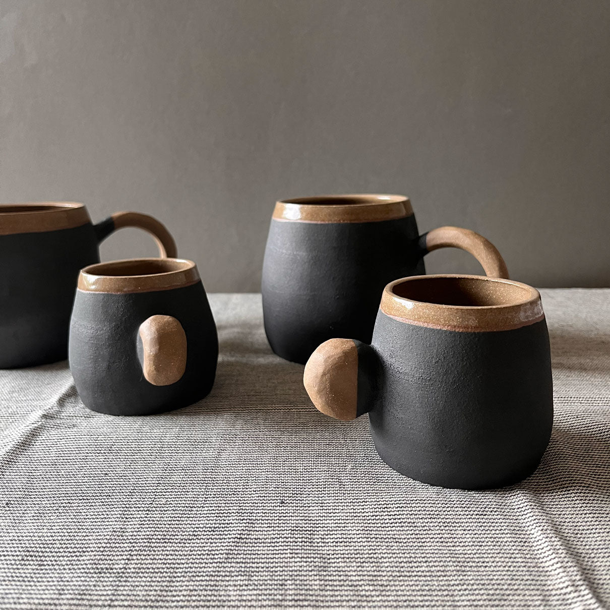 An elegant bulbous body form in brown stoneware, featuring a hammered raw texture. Black underglazed exterior that has a volcanic rock texture, with a clear glazed lip and interior.