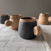An elegant bulbous body form in brown stoneware, featuring a hammered raw texture. Black underglazed exterior that has a volcanic rock texture, with a clear glazed lip and interior.