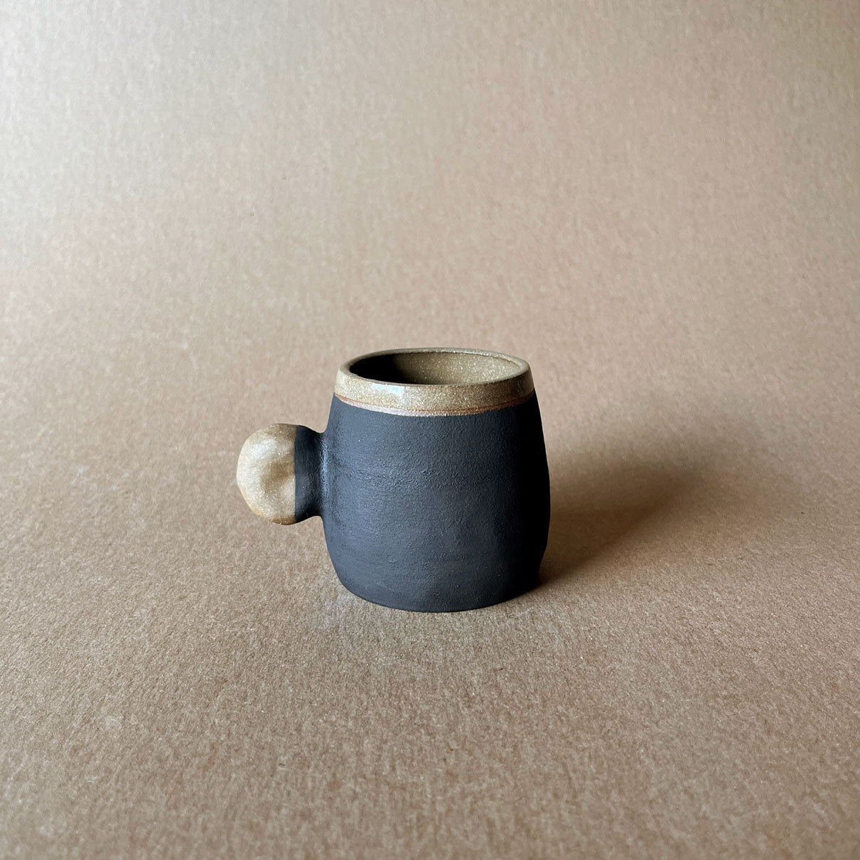An elegant bulbous body form in brown stoneware, featuring a hammered raw texture. Black underglazed exterior that has a volcanic rock texture, with a clear glazed lip and interior.