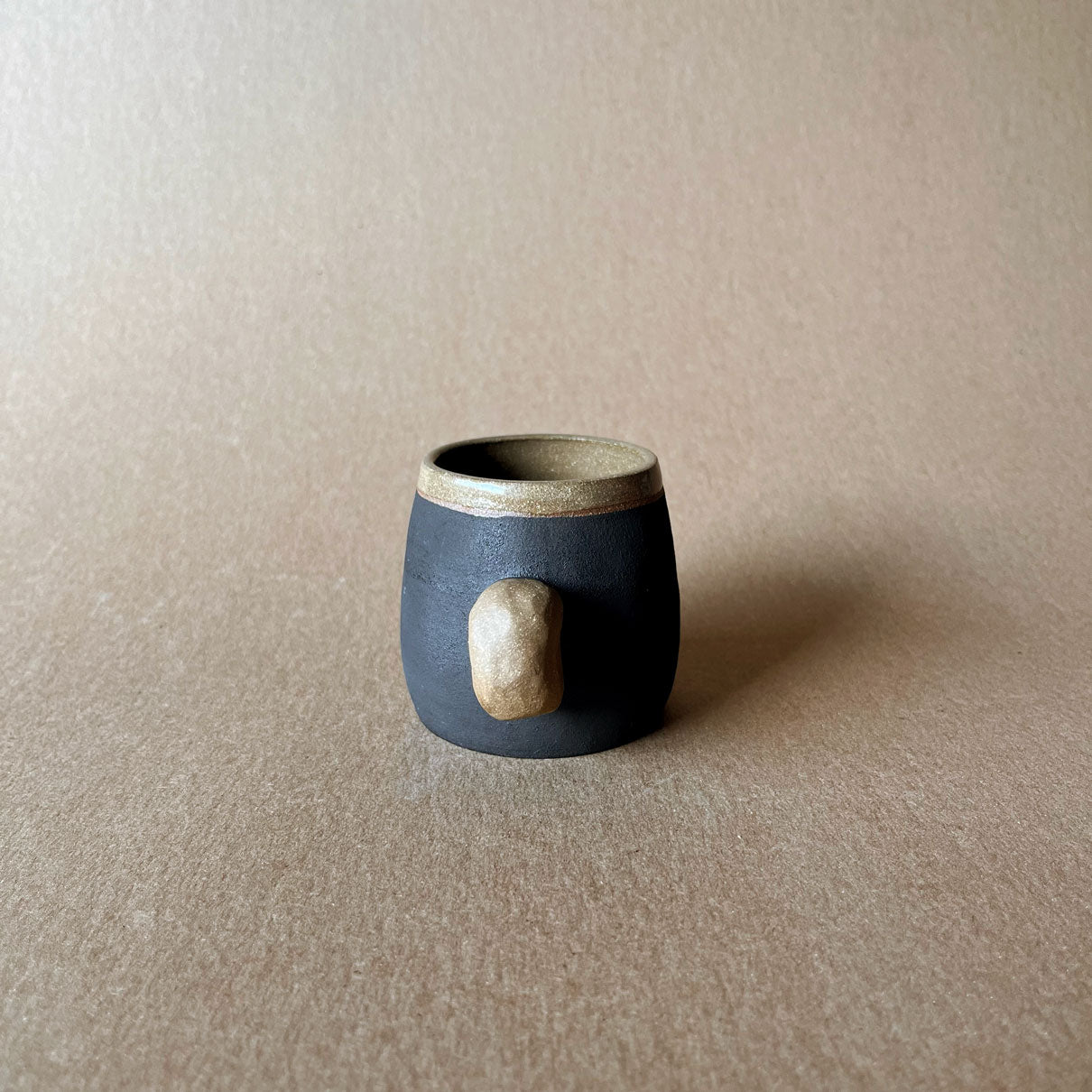 An elegant bulbous body form in brown stoneware, featuring a hammered raw texture. Black underglazed exterior that has a volcanic rock texture, with a clear glazed lip and interior.