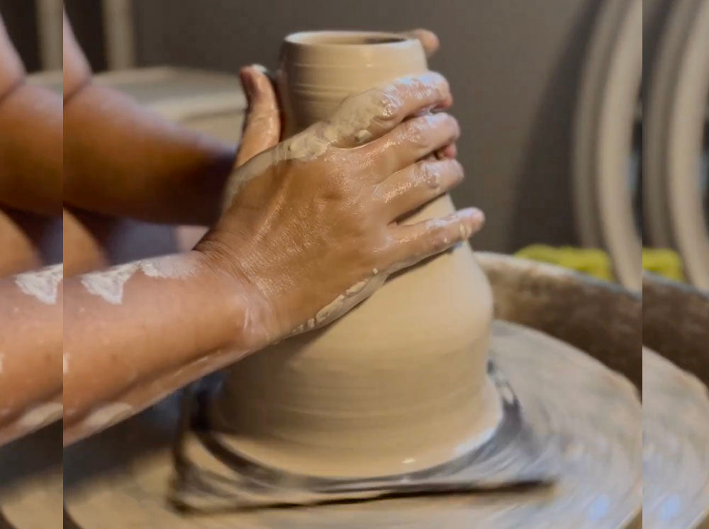 The hands of the maker in the process of throwing a ceramic item on the wheel.