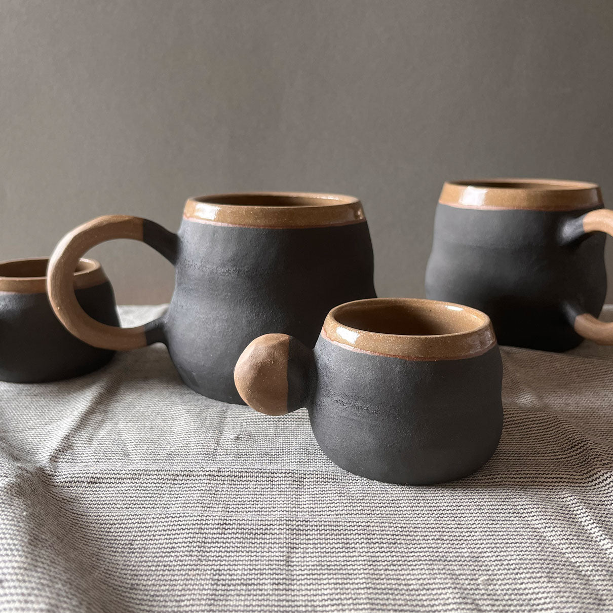Sombra Baza Mugs and Espresso cups, brown clay with round and double convex body shape, featuring a matte black glaze. 