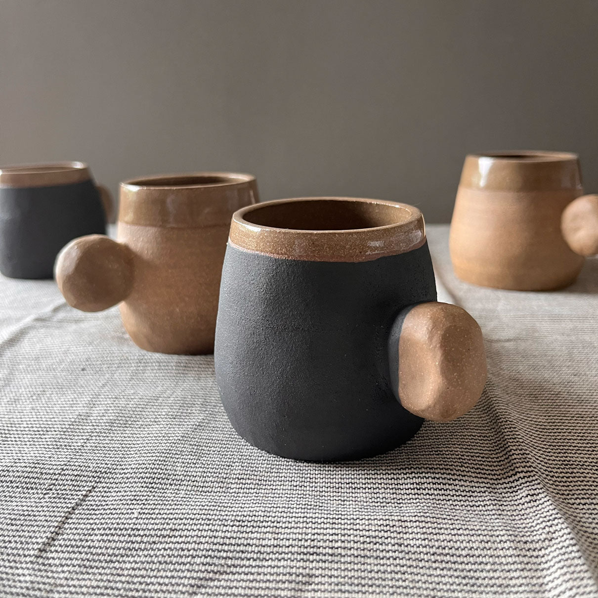 An elegant bulbous body form in brown stoneware, featuring a hammered raw texture. Black underglazed exterior that has a volcanic rock texture, with a clear glazed lip and interior. 