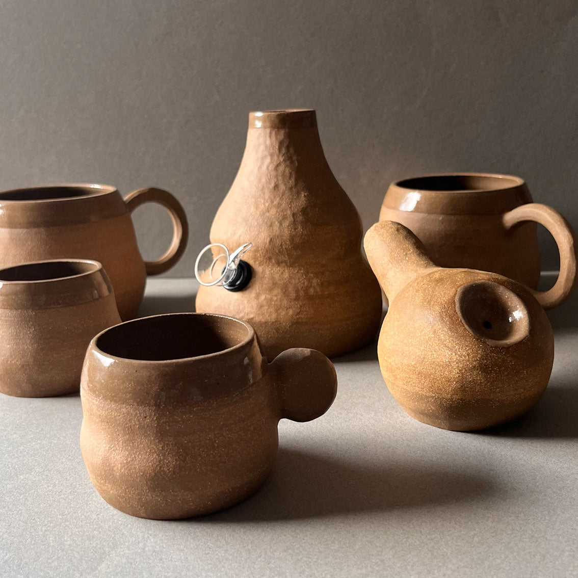 Terra Onda collection, brown clay bodies with hammered texture and clear glazed interiors. Mugs, Espresso cups, pipes and bongs