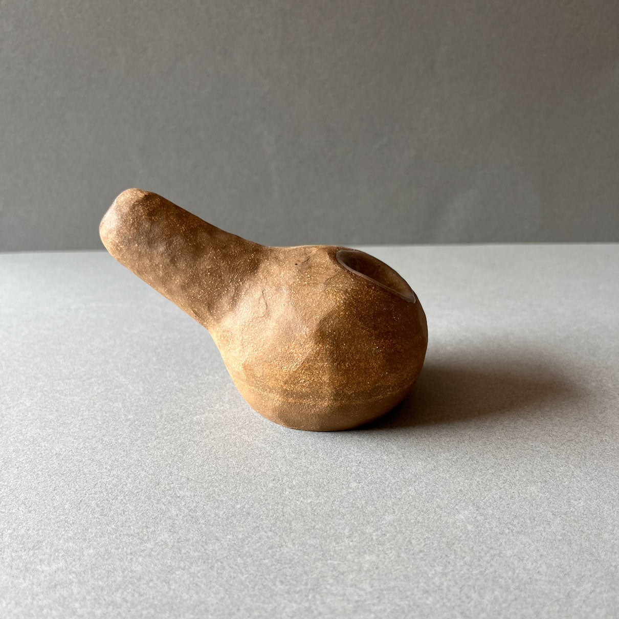 A gourd shaped, spherical body form in brown stoneware with hammered texture, featuring a large glazed inset bowl and rounded stem protrusion mouthpiece. 
