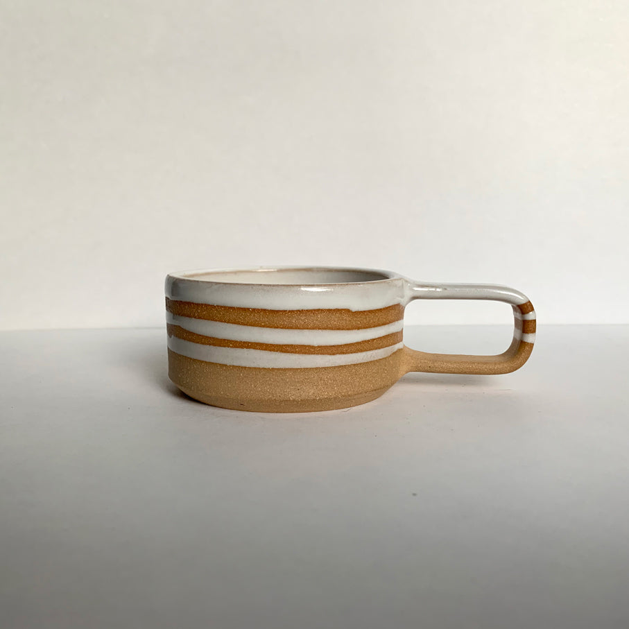 Brown stoneware espresso cup with glossy white interior and decorative stripes, side view
