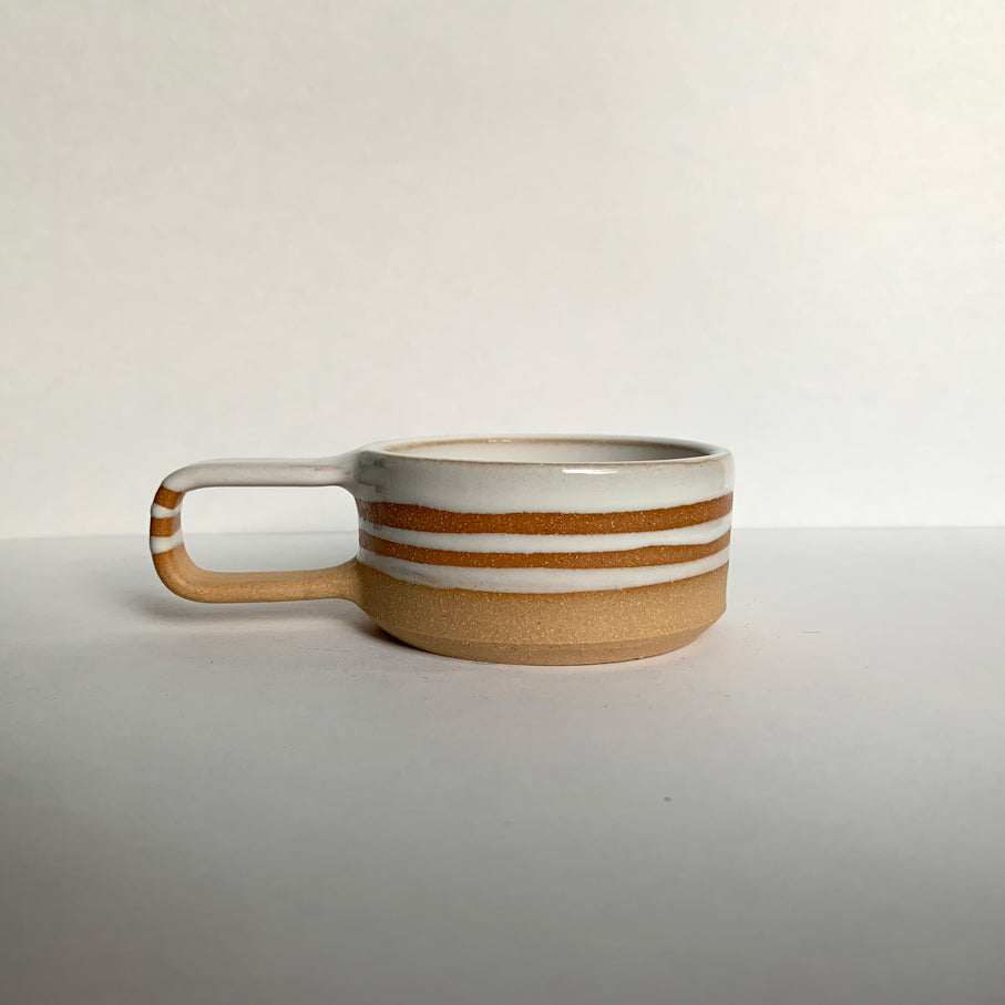 Brown stoneware espresso cup with glossy white interior and decorative stripes, side view